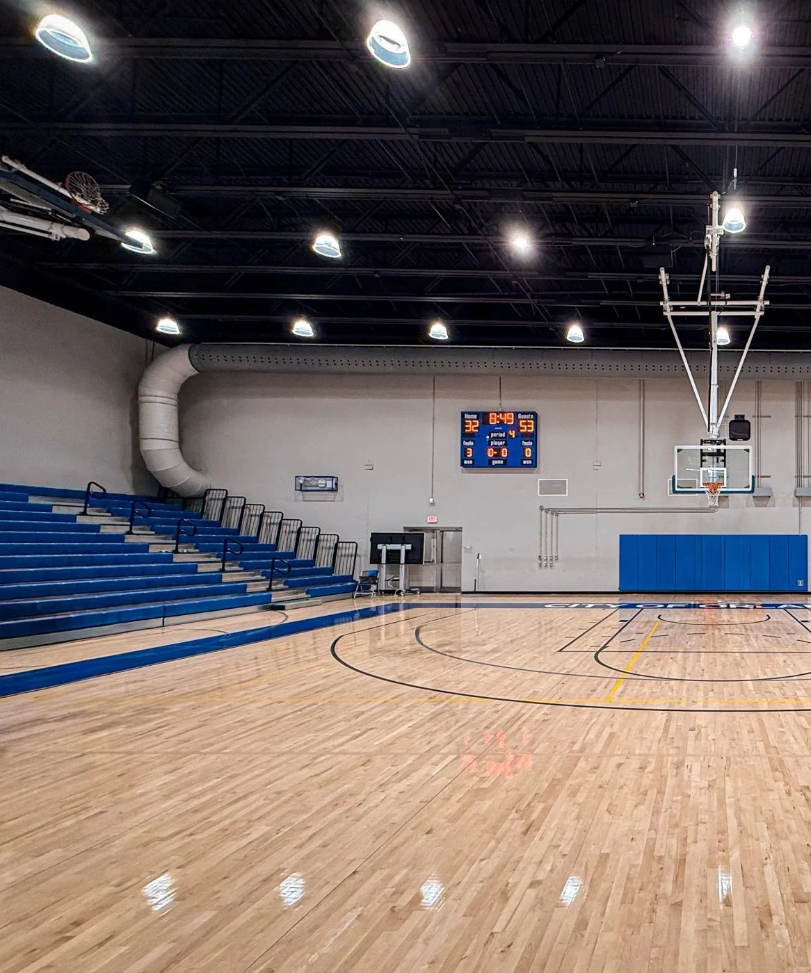 An empty sports hall before a session, with a polished wooden court and blue seating