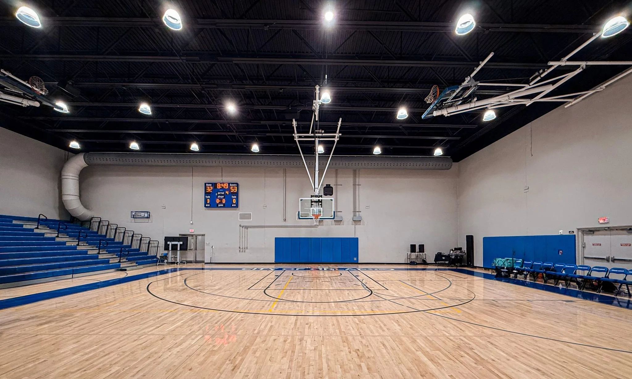 An empty sports hall before a session, with a polished wooden court and blue seating